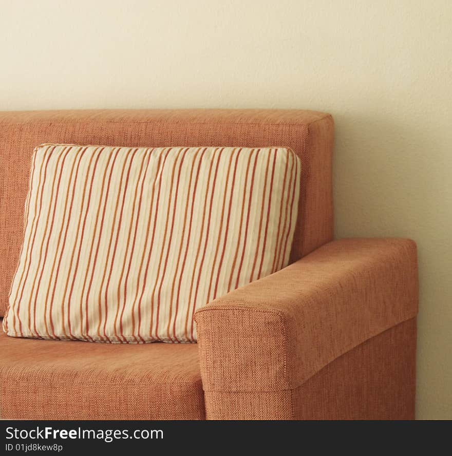 Orange sofa with a striped pillow set against a wall