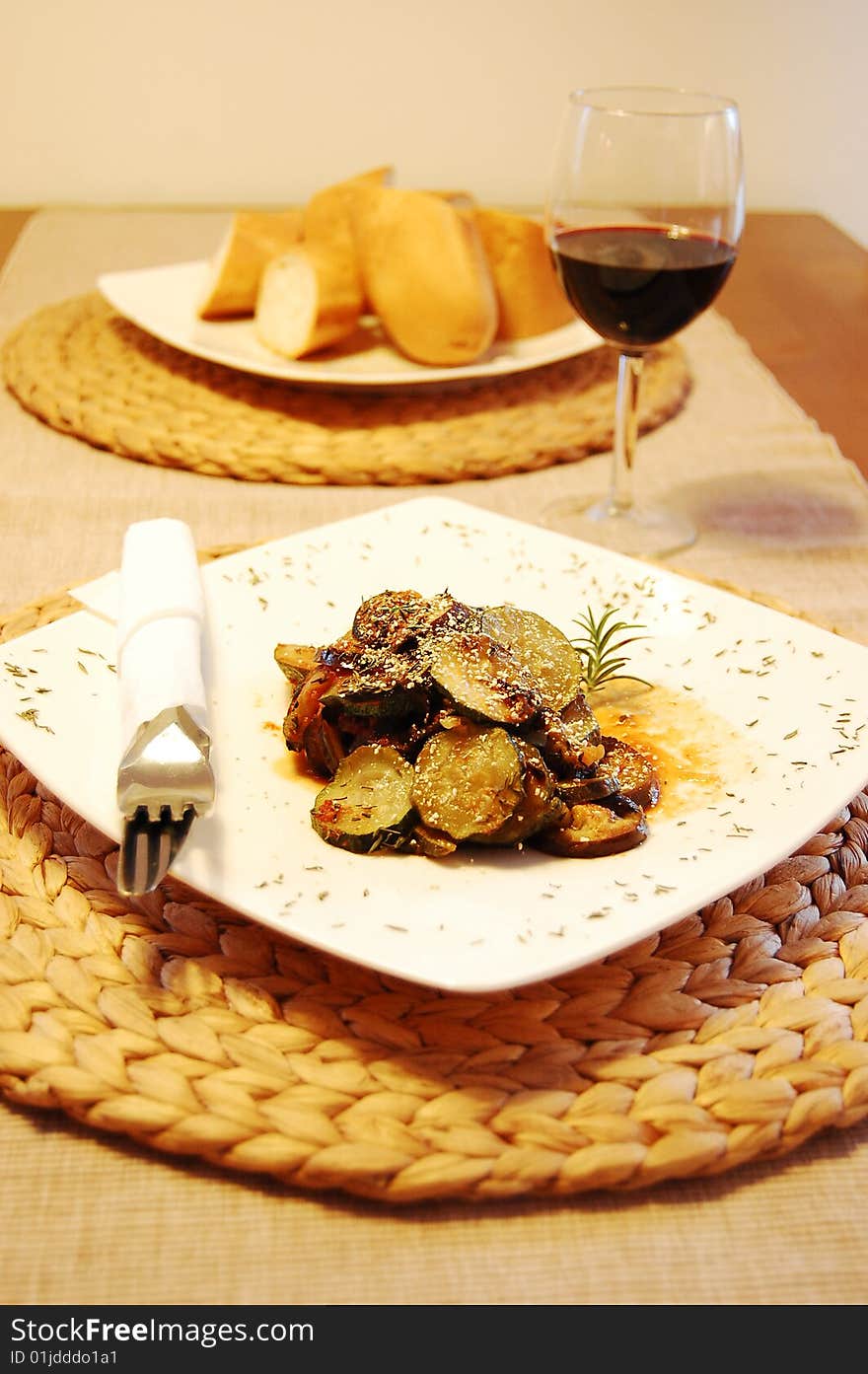 Ratatouille on a white plate, red wine and baguette added.