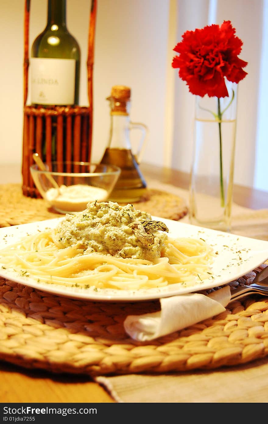 Pasta with broccoli on a white plate. Decorationn of red flower, bottle of wine and olive oil.