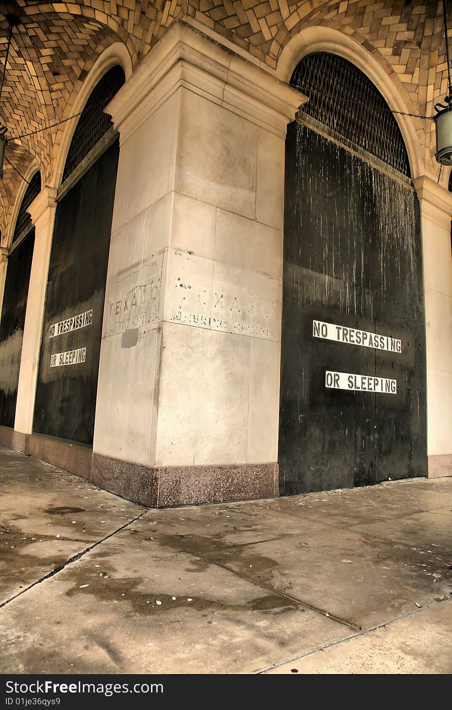 Wooden Doors Painted Blacked with words saying no trespassing or sleeping between white granite columns on floor