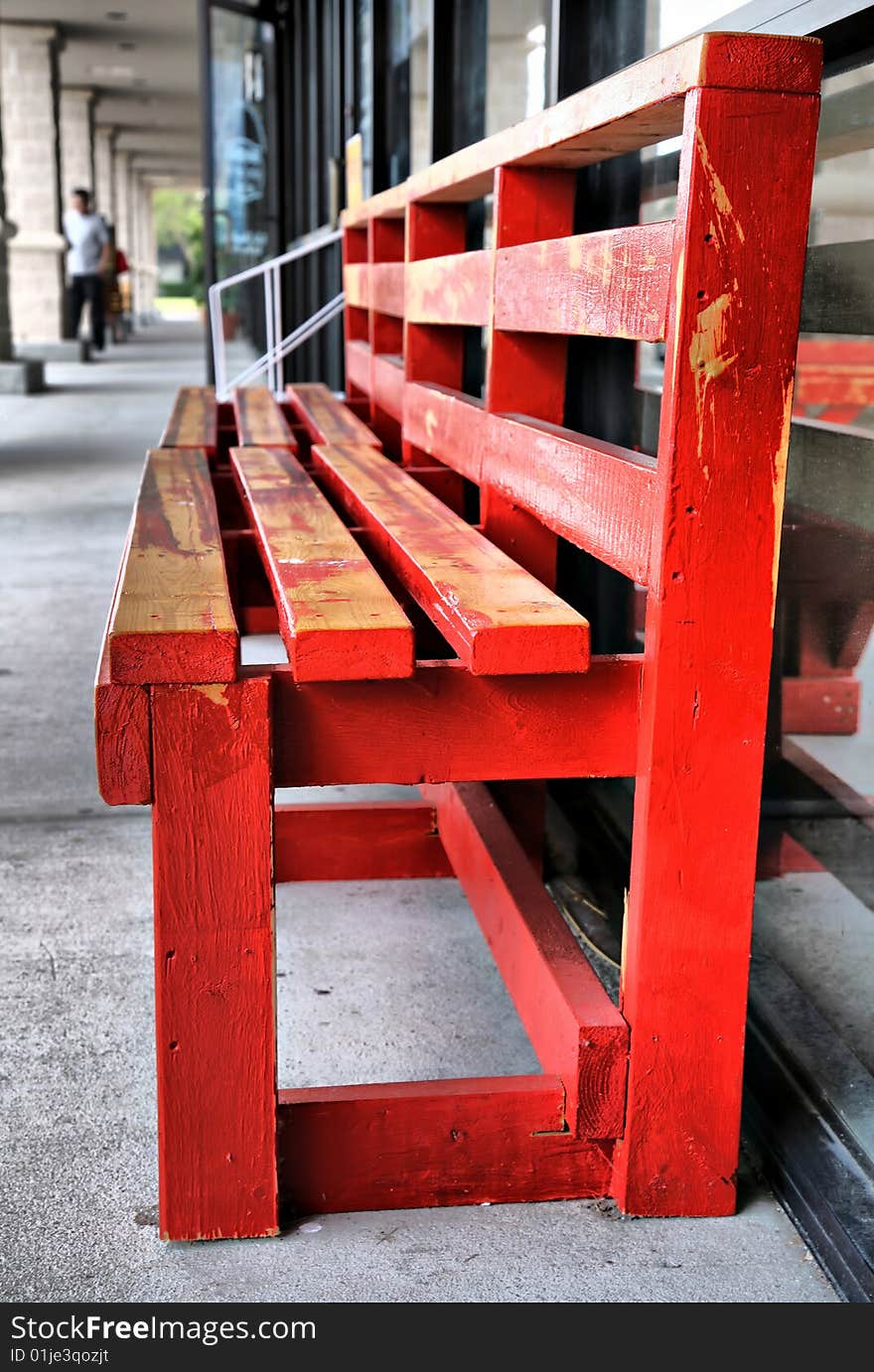 Red Bench in perspective with grainy painted wood and people in backgroun