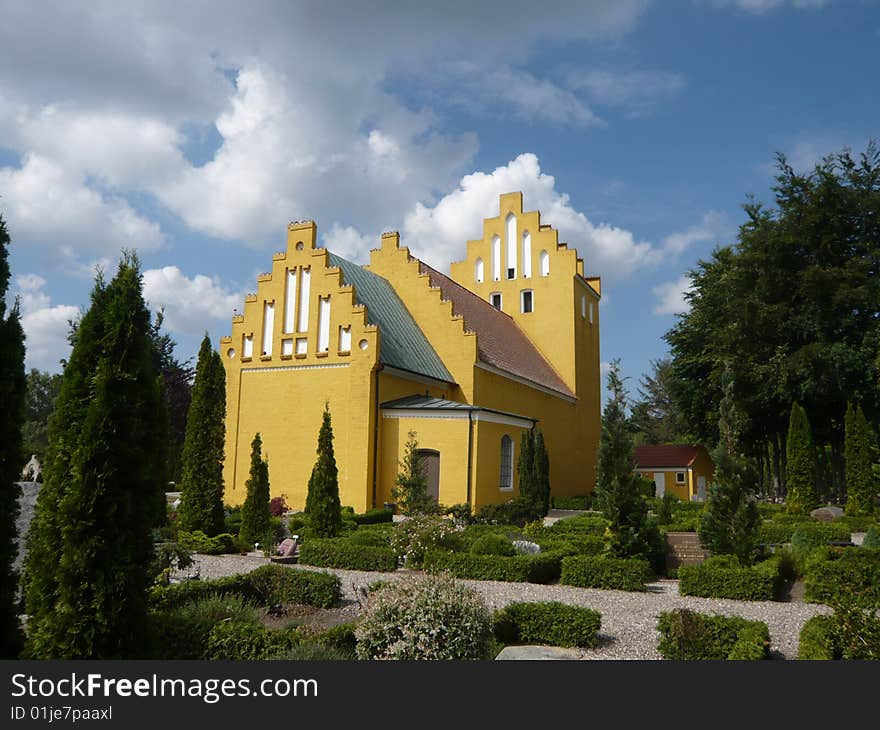 Yellow danish christian church with clouds matching the tower