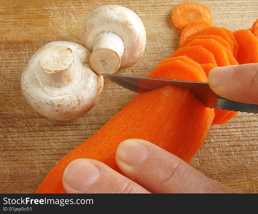 Hands cut carrot on the kitchen board with some mushrooms. Hands cut carrot on the kitchen board with some mushrooms