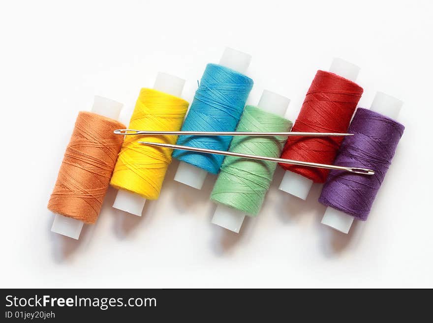 Spools of variegated thread with needles lying on white background. Spools of variegated thread with needles lying on white background