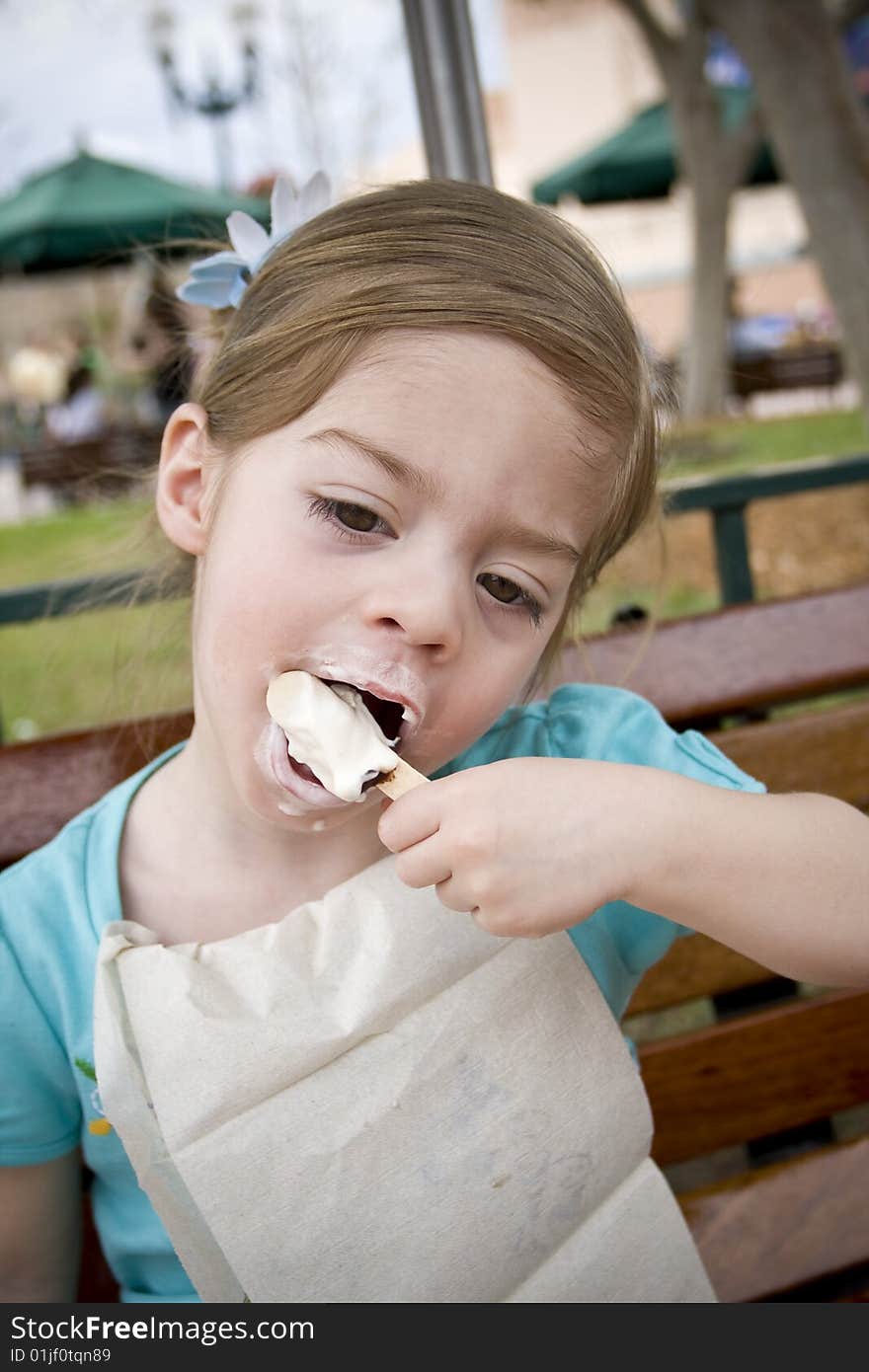 A cute little girl eats her ice cream treat at the park and gets a bit messy in the process. A cute little girl eats her ice cream treat at the park and gets a bit messy in the process