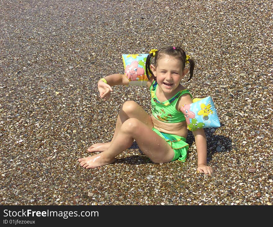 A girl in a green swimming suit plays the bank near water. A girl in a green swimming suit plays the bank near water.