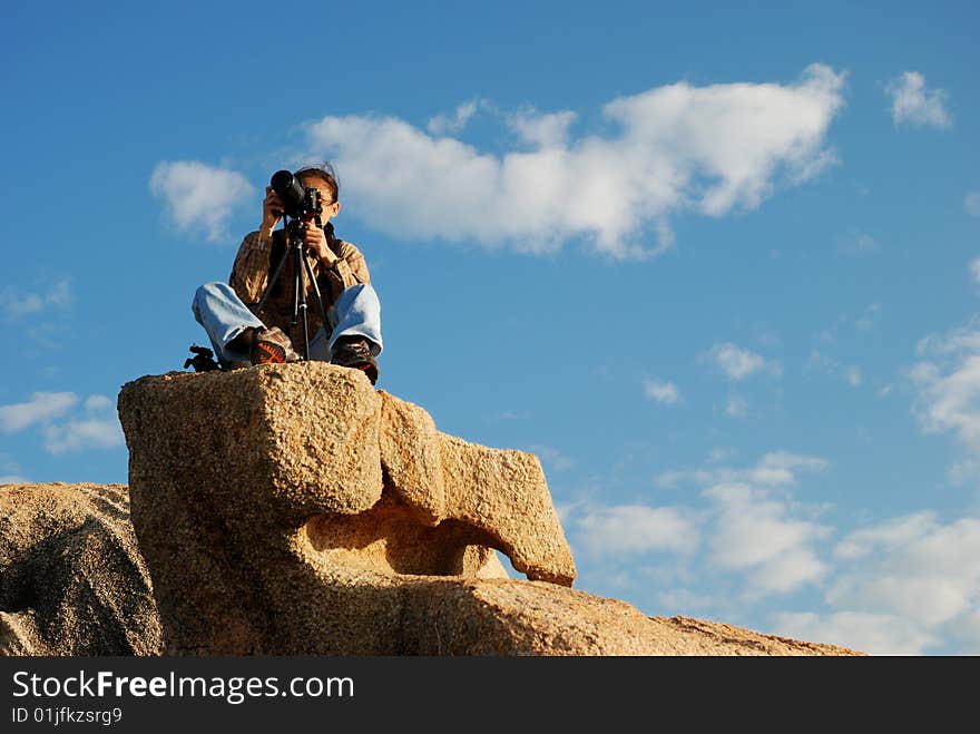 Photographer seated on a Big Rock against blue Sky. Photographer seated on a Big Rock against blue Sky