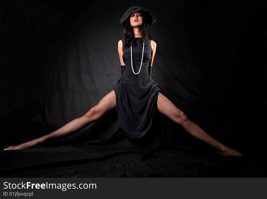 Girl with long legs in hat with veil and perl against black background