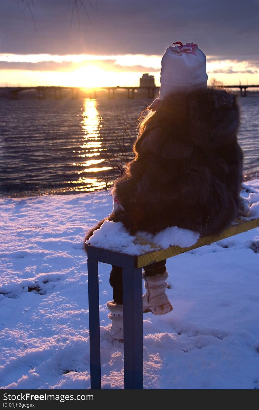 Little girl sitting on bench look at winter sunset. Little girl sitting on bench look at winter sunset