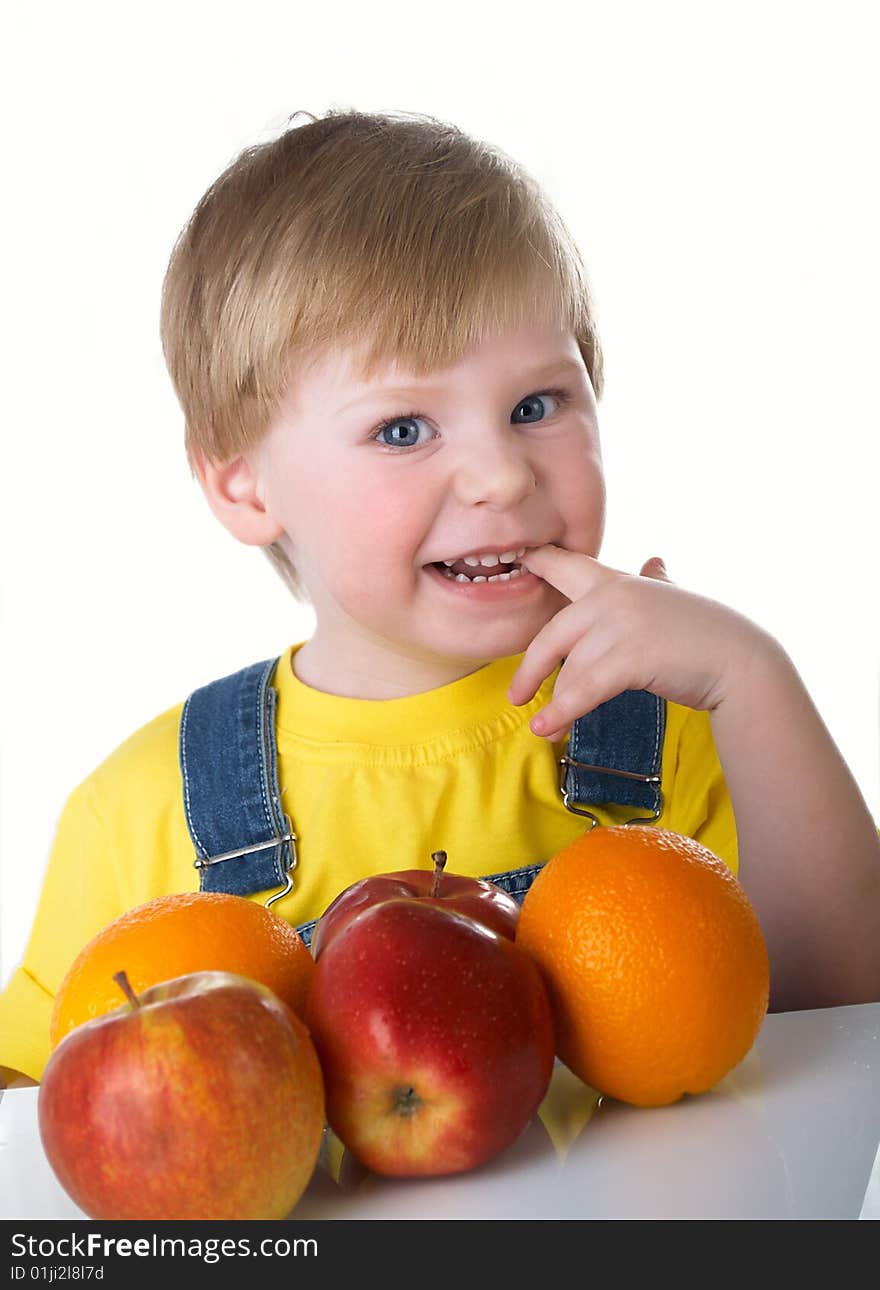 The child sits on a table with fruit. The child sits on a table with fruit