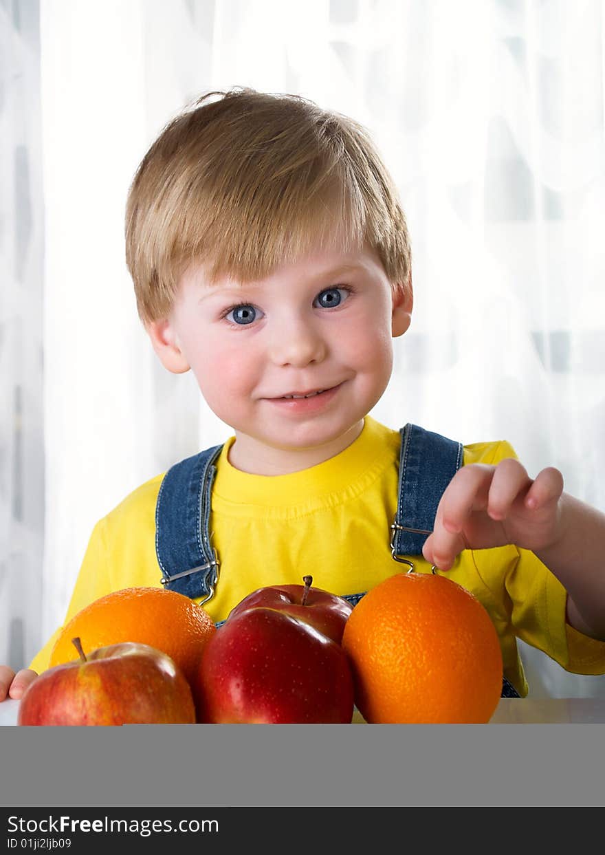 The child sits on a table with fruit. The child sits on a table with fruit