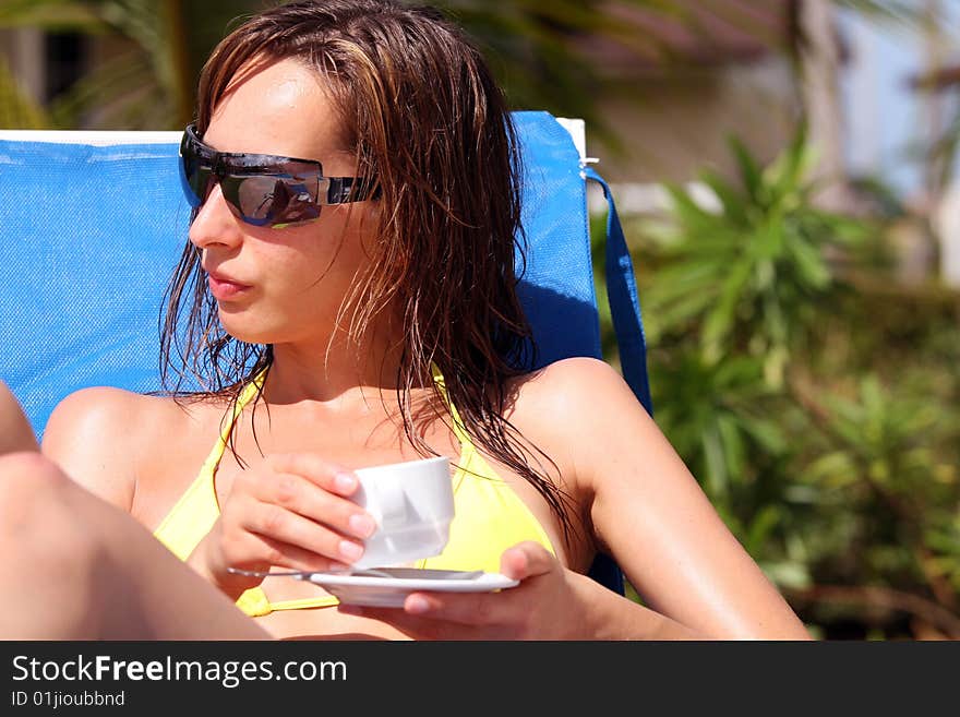 Woman sitting in chaise and drinking cup coffee by the pool. Woman sitting in chaise and drinking cup coffee by the pool