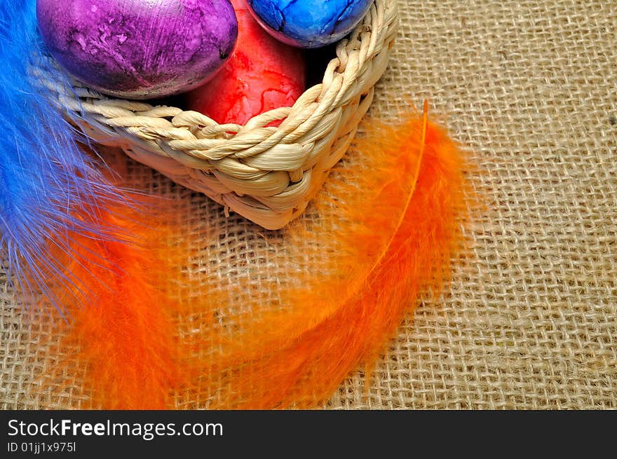 Colorful Easter eggs in basket with feathers hanging around.