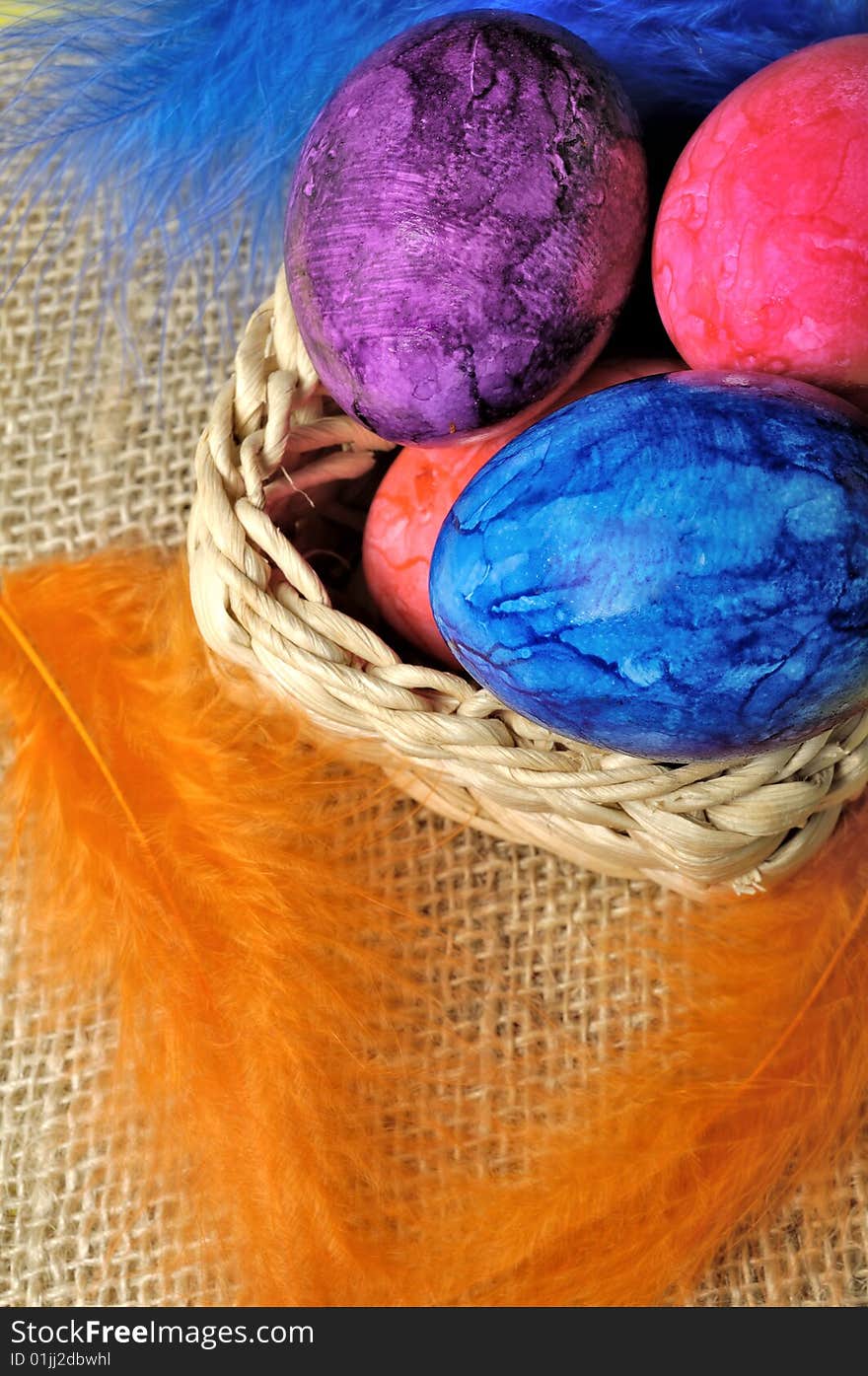 Colorful Easter eggs in basket with feathers hanging around.