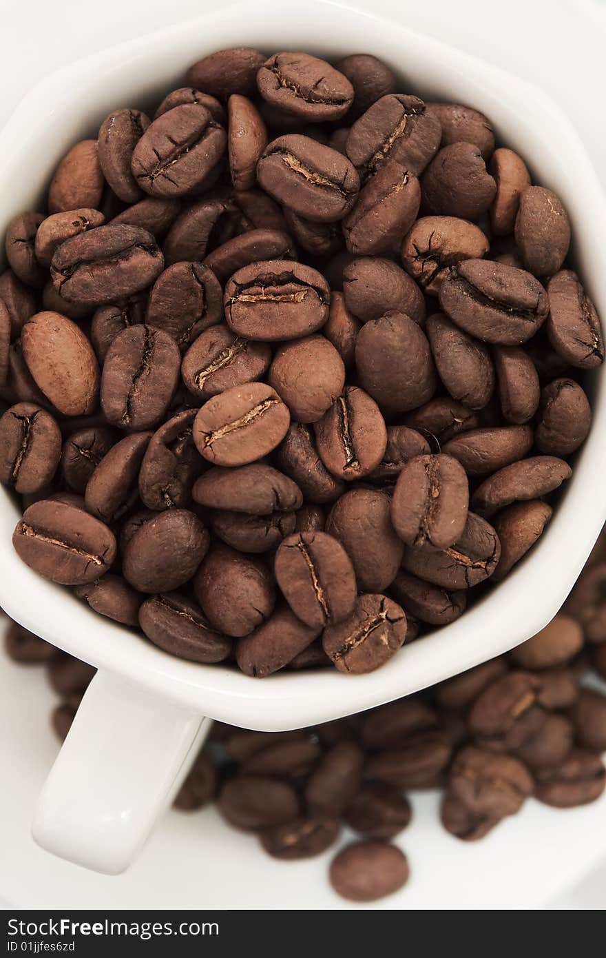 Coffee cup filled with coffee beans, and coffee beans scattered over a plate. Coffee cup filled with coffee beans, and coffee beans scattered over a plate