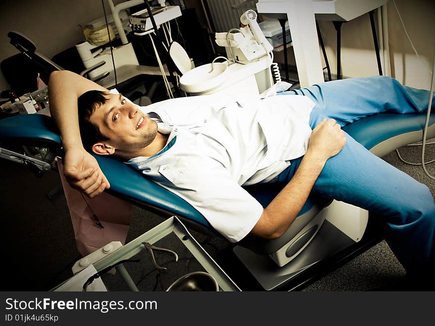 Young man (a dentist or a patient) lies on the chair in the dentist's office in a very relaxed pose ans smiles. Young man (a dentist or a patient) lies on the chair in the dentist's office in a very relaxed pose ans smiles