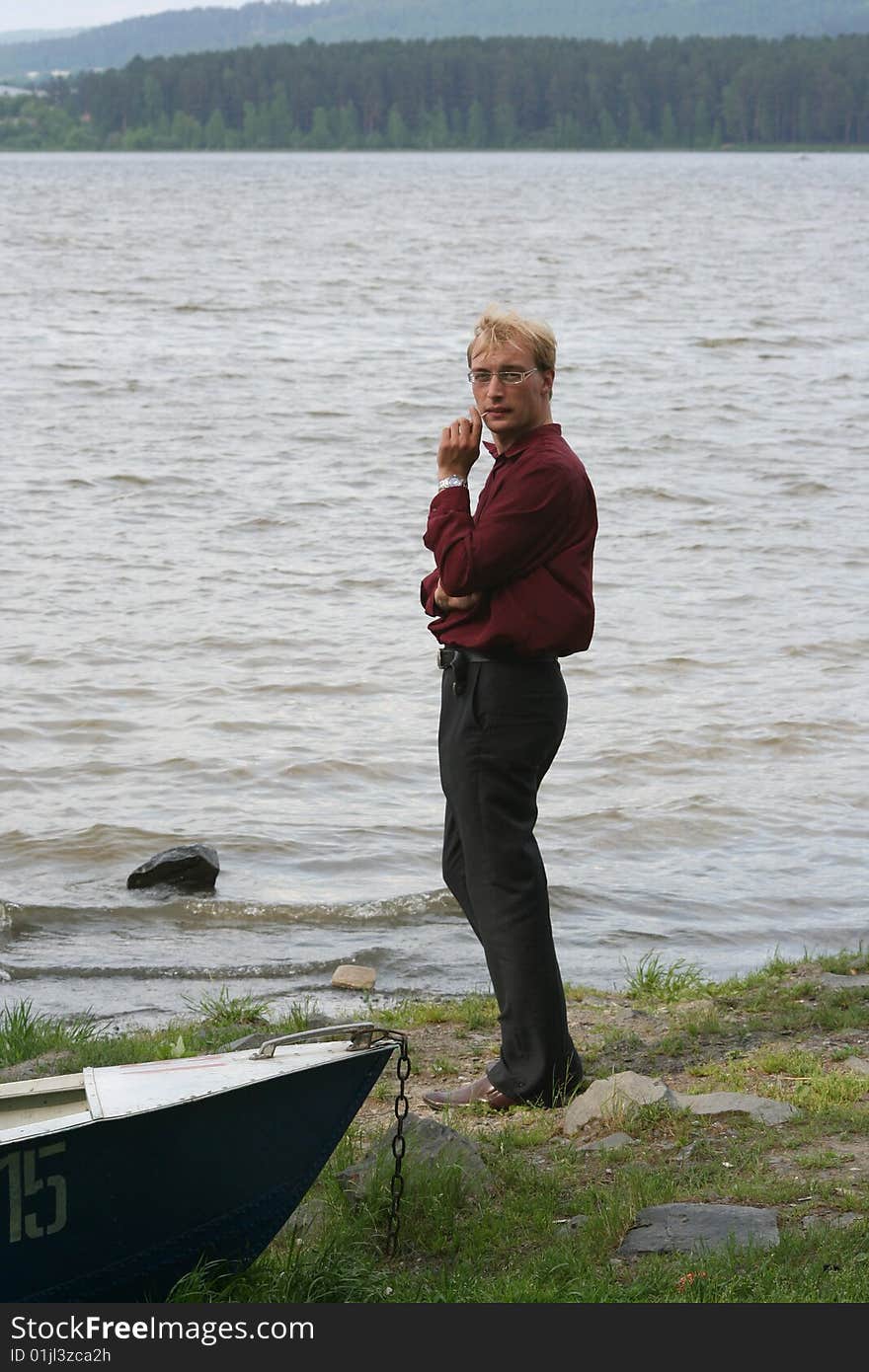 A young man stands at a lake next to a boat. A young man stands at a lake next to a boat