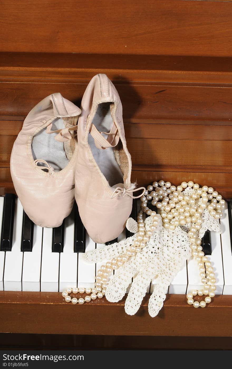 Ballet shoes, lace glove and pearls on a piano keys