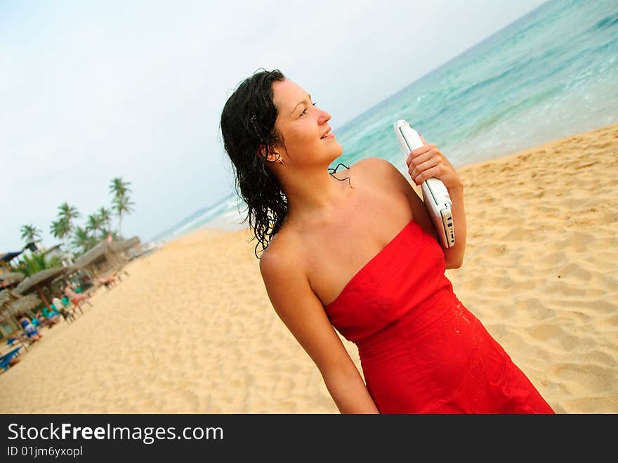 Beautiful young woman walking with laptop on the beach. The sun is setting and light is moody, she�s smiling and content after good days work. Beautiful young woman walking with laptop on the beach. The sun is setting and light is moody, she�s smiling and content after good days work.