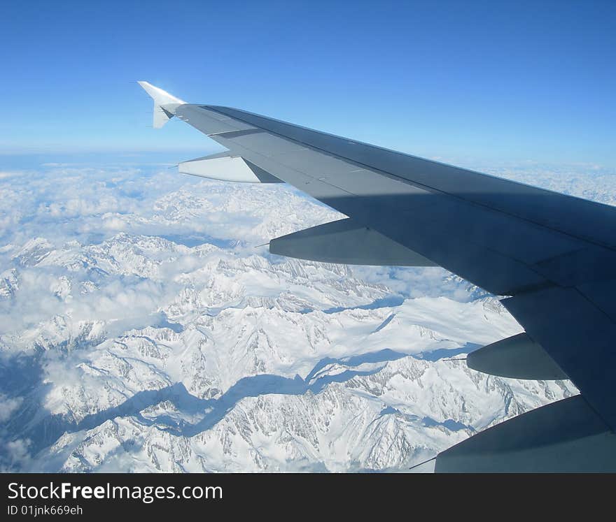 Flying over the Alps - view of airplane wing over snow capped mountains