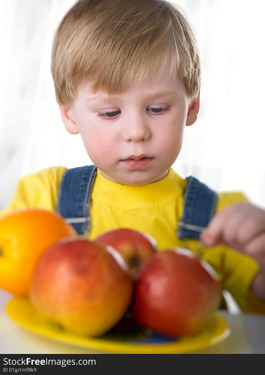 The child sits on a table with fruit. The child sits on a table with fruit