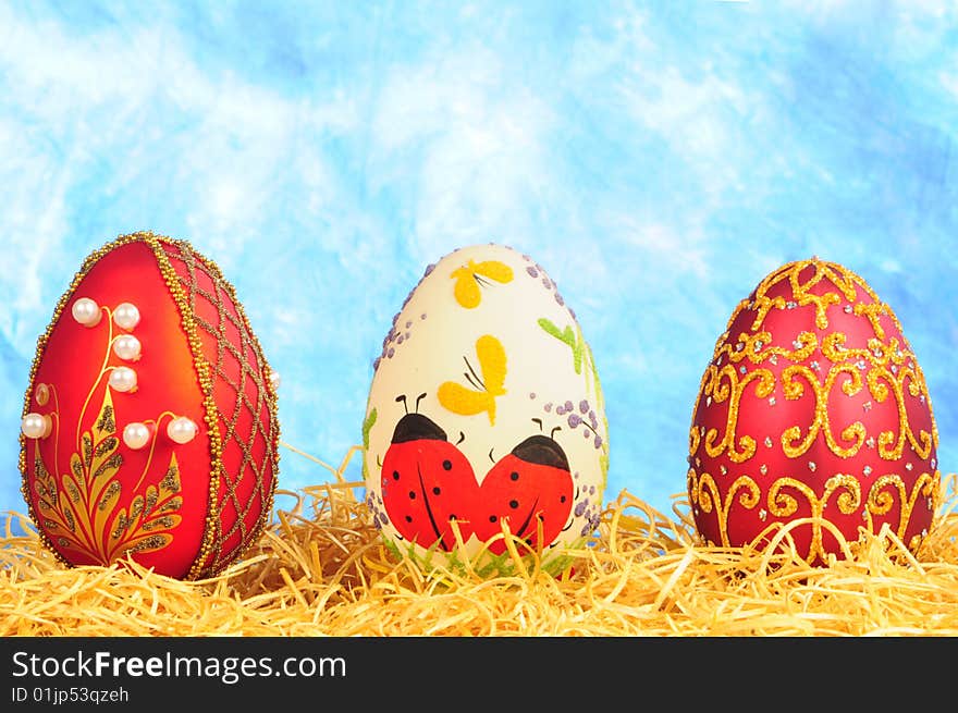 Three luxury easter eggs in straw on blue background