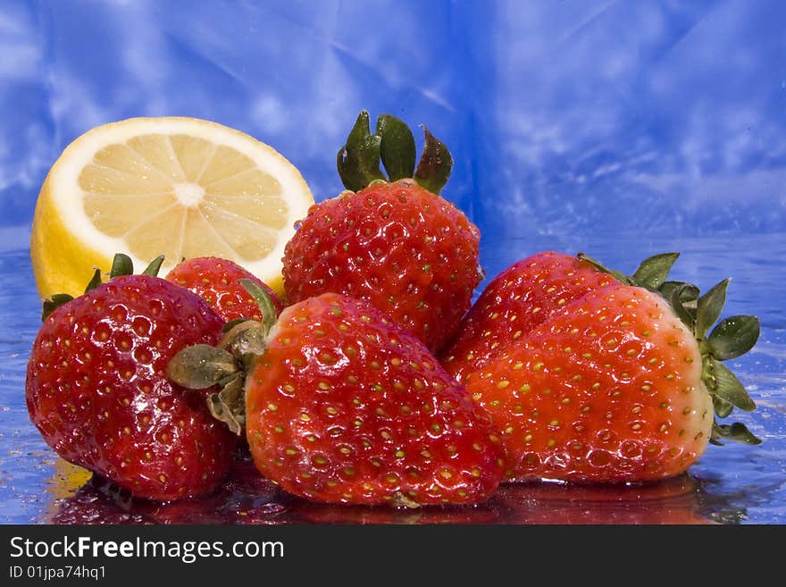 Several wet strawberries and lemon with blue background