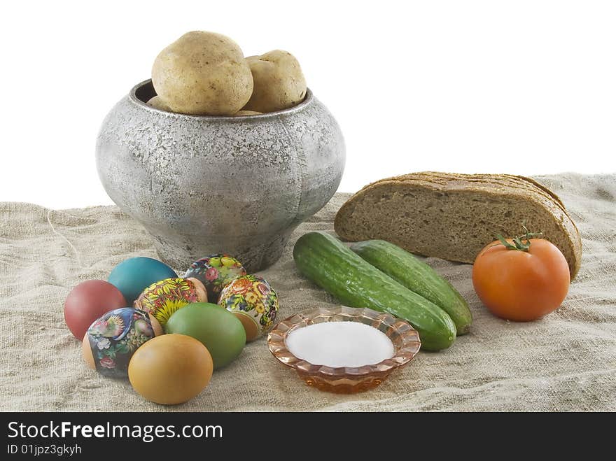 Still-life from vegetarian food. Fresh eggs lying in a wattled small basket, fragrant rye bread, a boiled potato in a pig-iron kettle, a saltcellar on a rough fabric