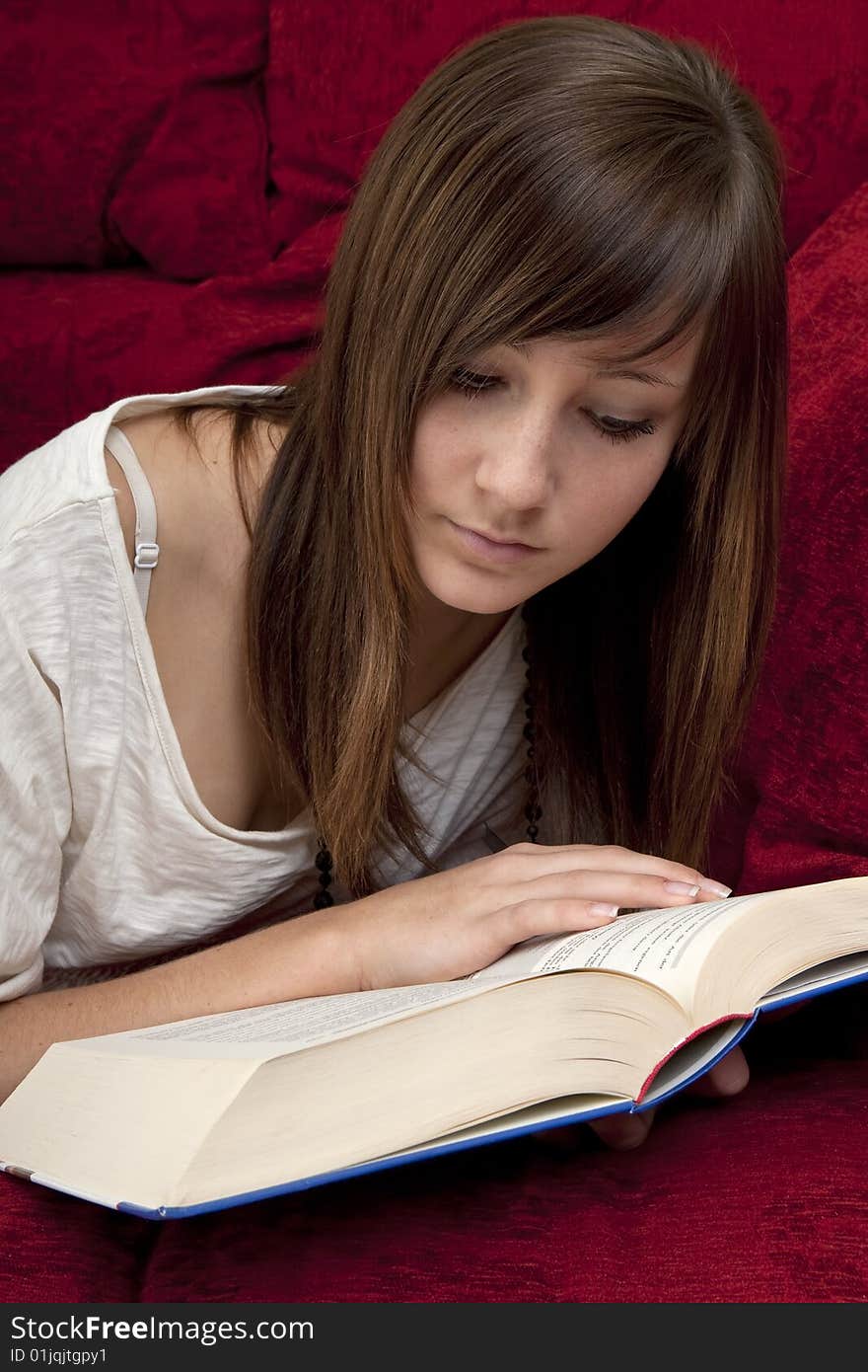 Female teenager reads book, lying on a red bench