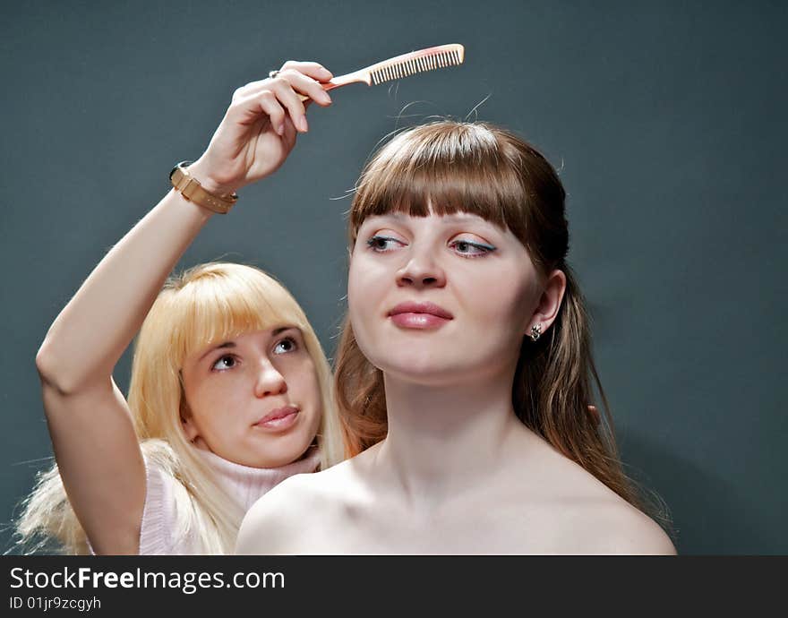 A blonde girl combing another girls` hair. A blonde girl combing another girls` hair