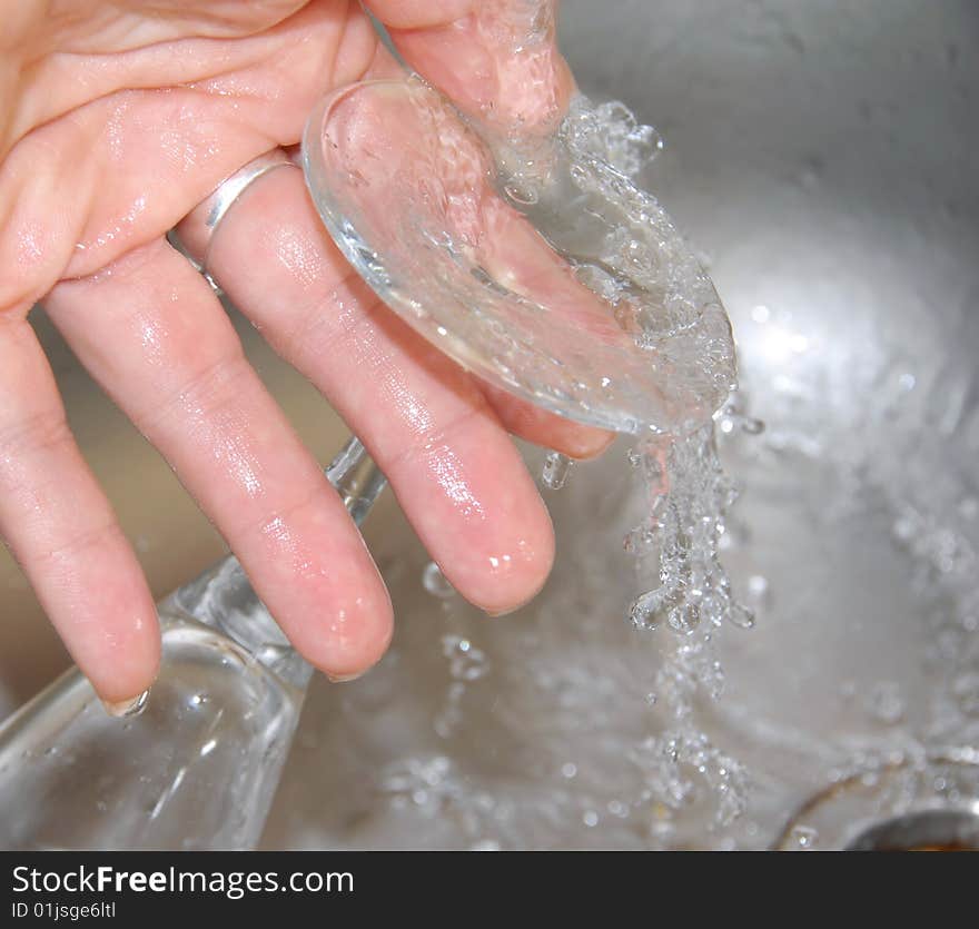 Hand washing wineglass in water in sink. Hand washing wineglass in water in sink