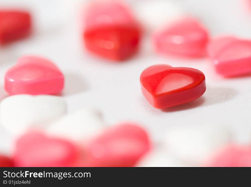 Heart shaped candy in focus, standing out amongst other candies. On white background. Candies are red, pink and white. Heart shaped candy in focus, standing out amongst other candies. On white background. Candies are red, pink and white.