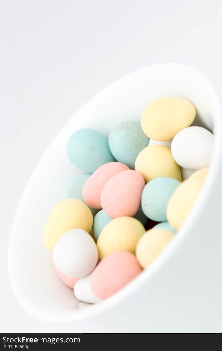 Pastel colored egg shaped candies in white bowl, on white background. There are pink, yellow, green, blue and white ones. Pastel colored egg shaped candies in white bowl, on white background. There are pink, yellow, green, blue and white ones.