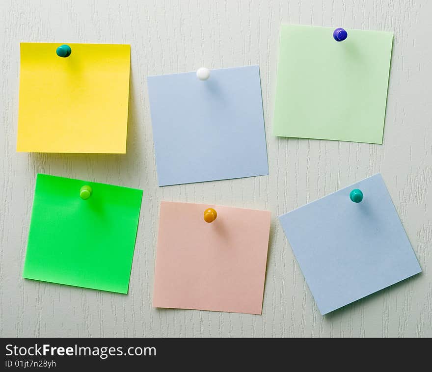 Message board for reminders. Sheets of different-colored pins are attached to a light wooden surface. Message board for reminders. Sheets of different-colored pins are attached to a light wooden surface.