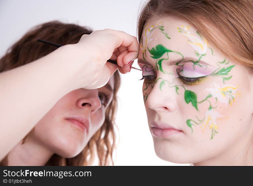 An artist drawing a colorfull flower with green white and yellow on the face of her model. An artist drawing a colorfull flower with green white and yellow on the face of her model