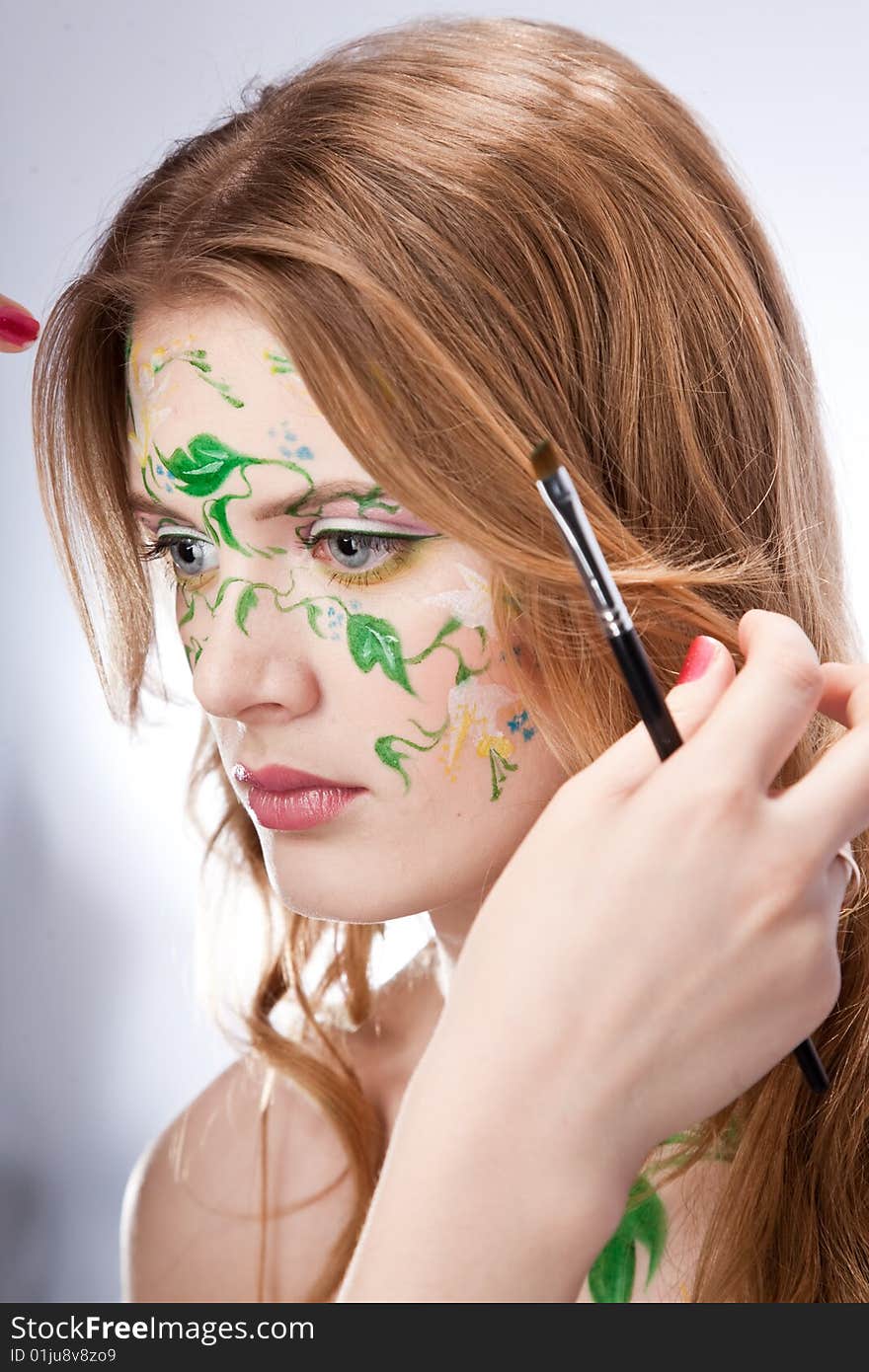 A beautiful young woman with a picture on her face and a hand of the artist. A beautiful young woman with a picture on her face and a hand of the artist