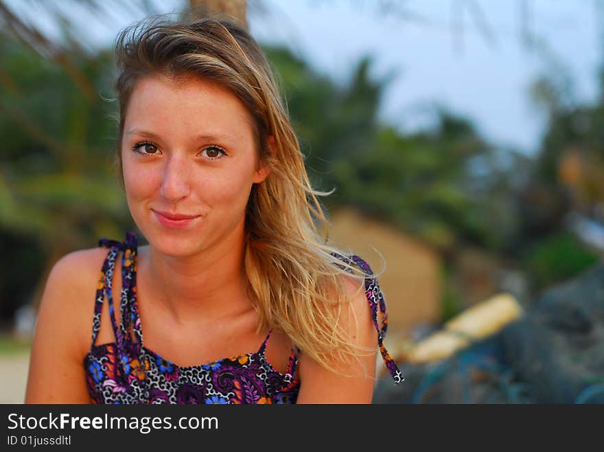 Beautiful, smiling young blond girl sitting on tropical beach with fishing nets in background. Beautiful, smiling young blond girl sitting on tropical beach with fishing nets in background.