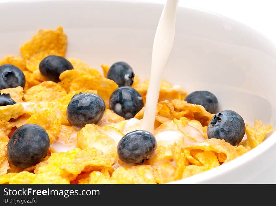 Horizontal view of pouring white milk into a bowl of breakfast flakes with blueberries