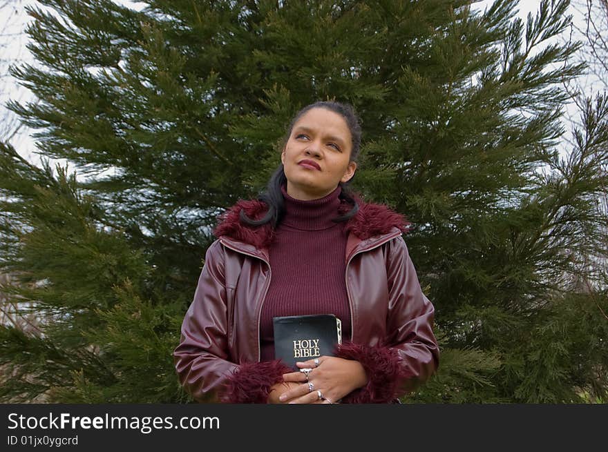 Young multi ethnic woman in late 20's in holding a bible while outside.  Contemplating and thoughtful is her expression. Young multi ethnic woman in late 20's in holding a bible while outside.  Contemplating and thoughtful is her expression.