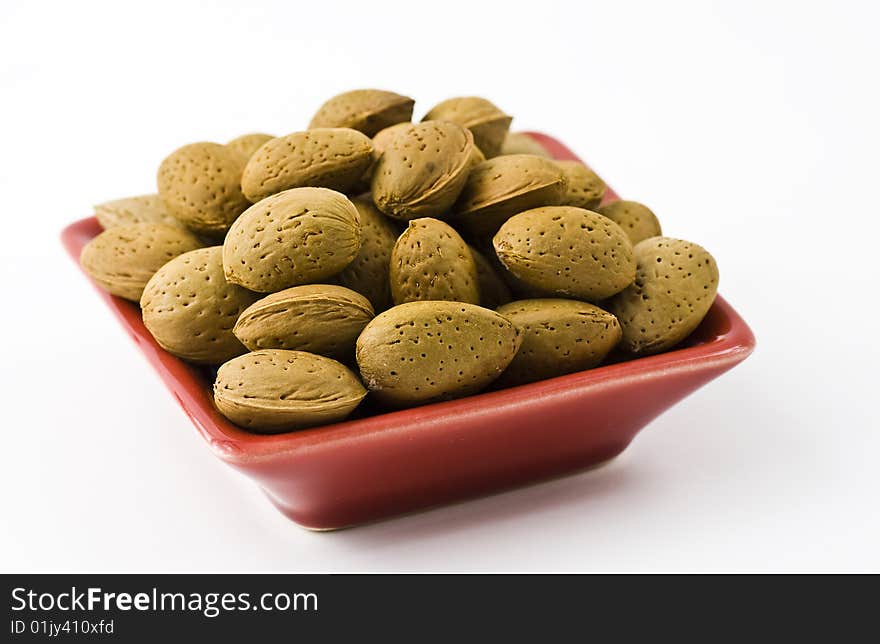 Handful of almonds in the red saucer isolated on the white background