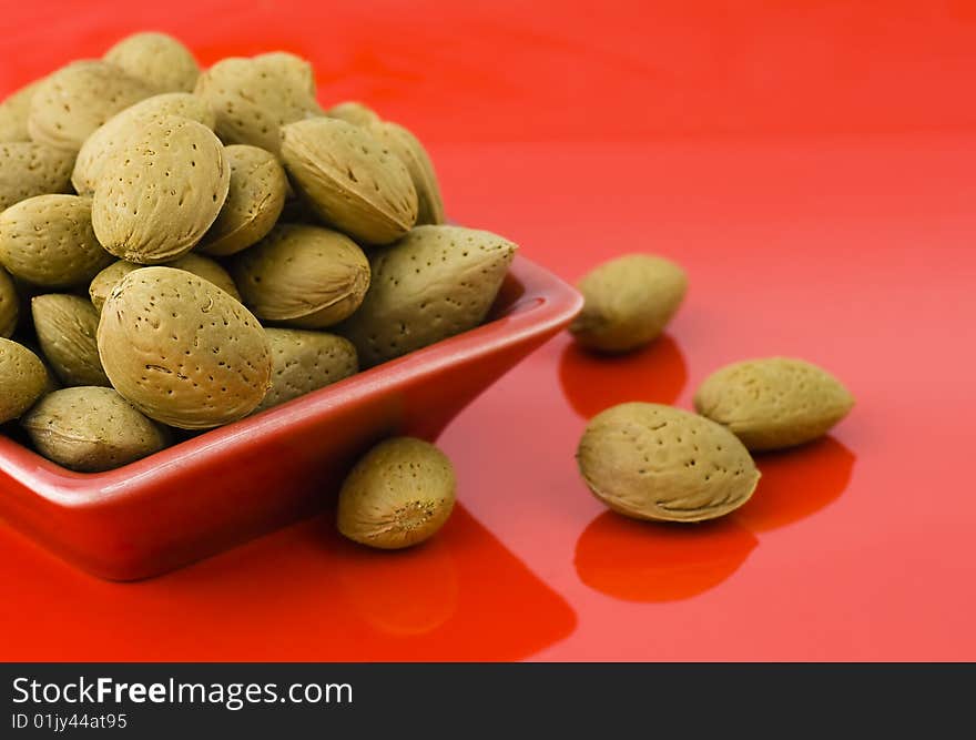 Handful of almonds in the red saucer isolated on the red background and some scattered