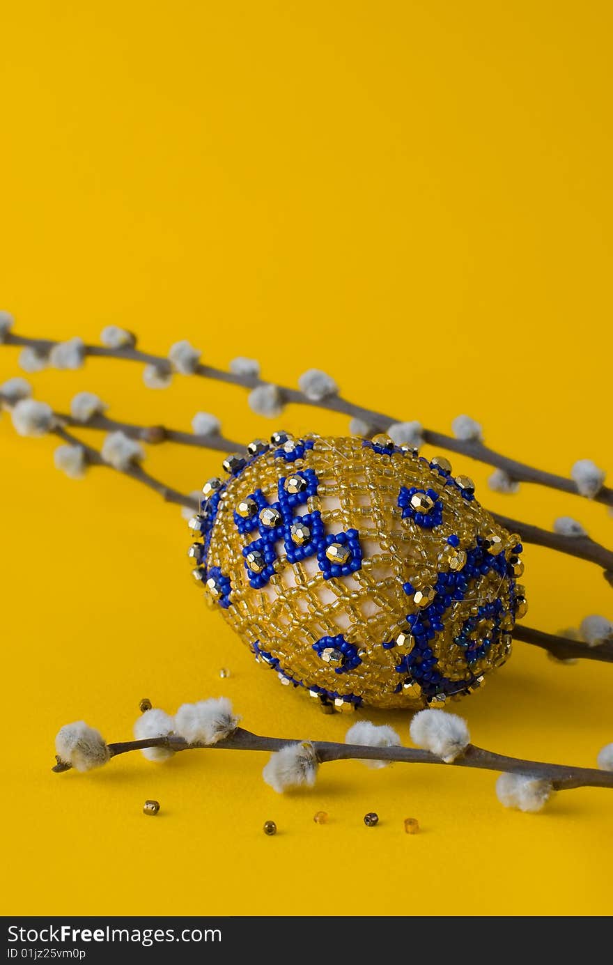 Bead easter egg and sprigs of pussy-willow on a yellow background. Bead easter egg and sprigs of pussy-willow on a yellow background