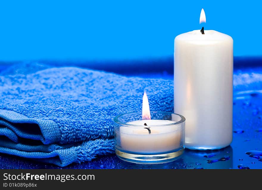 Spa essentials, candles and towel on blue background