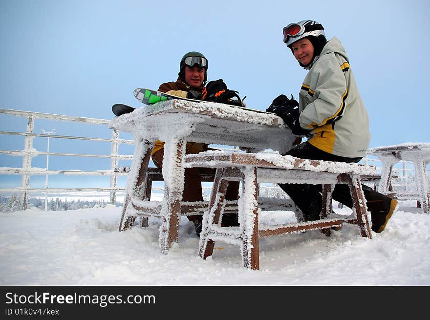 Couple of snowboarders sitting on the frozen bench