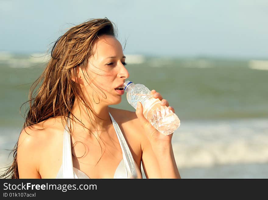 Woman drinking water on the beach by sunset