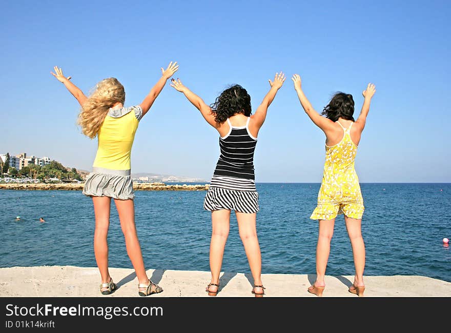 Three pretty girls hands up at the sea.