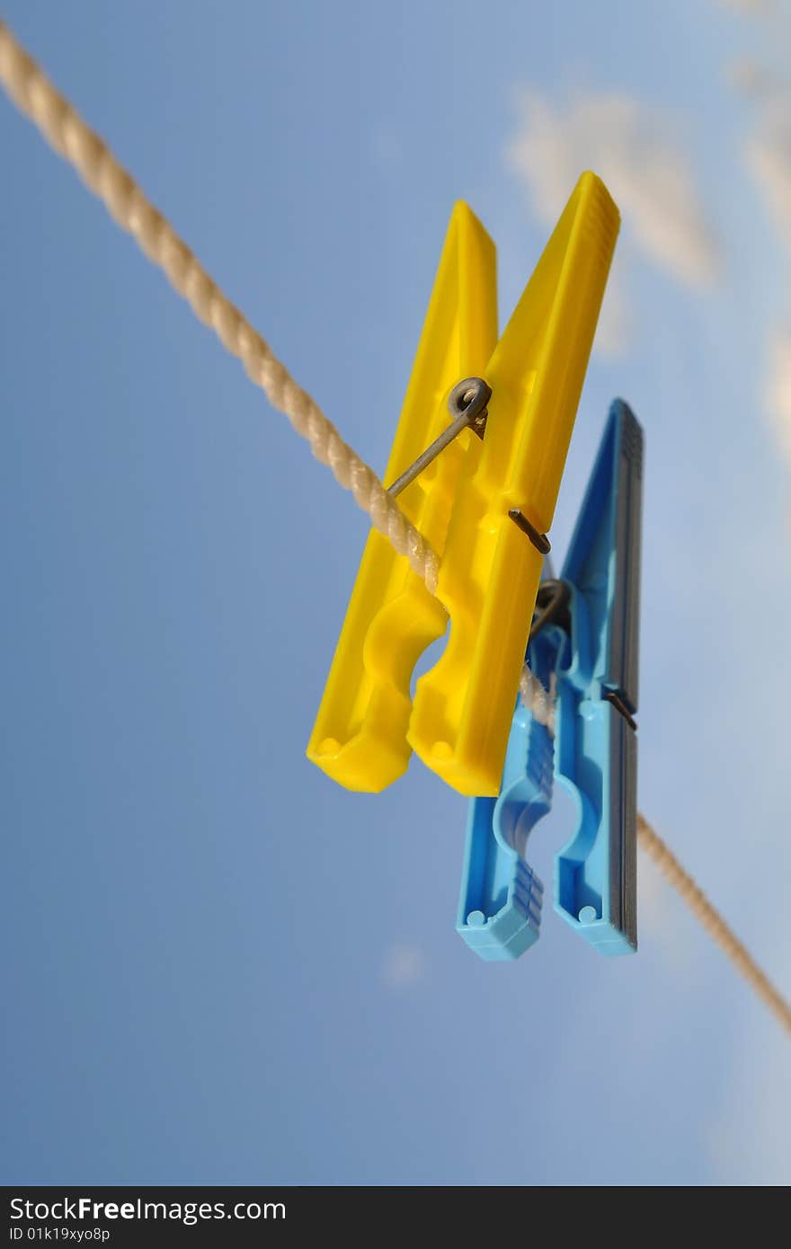 A pair of blue & yellow laundry clips against blue sky. A pair of blue & yellow laundry clips against blue sky.