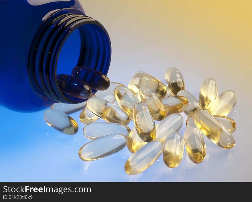 Orange capsules pouring out of a blue bottle on orange and blue background. Orange capsules pouring out of a blue bottle on orange and blue background