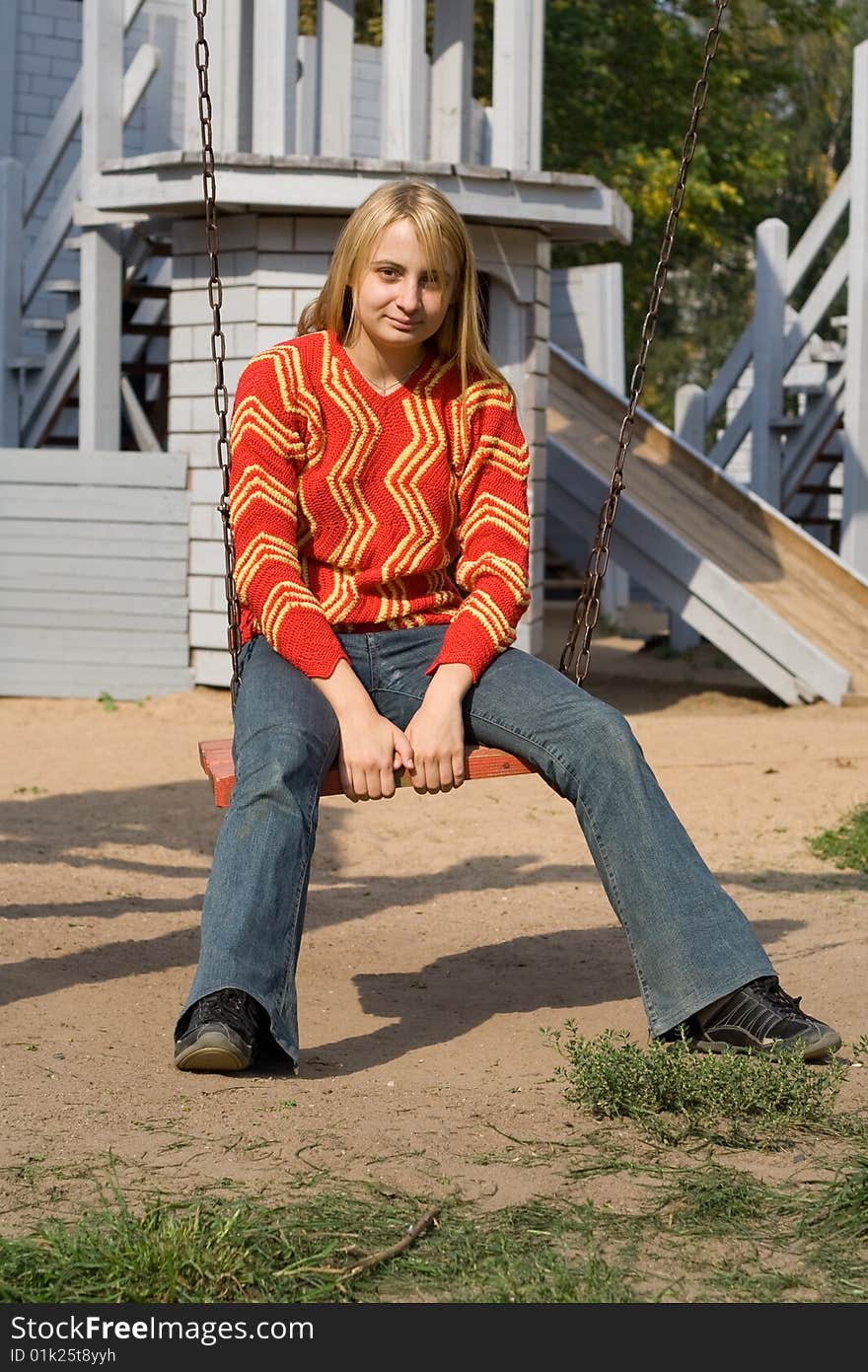 Girl in red pullover sitting on swing