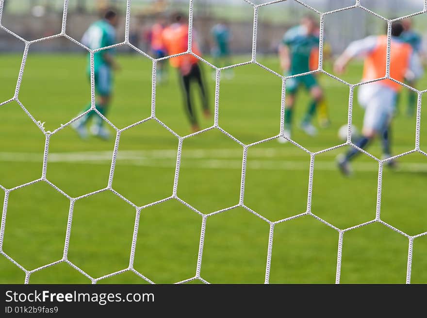 Football ground and football players through a grid of gate - an abstract dim background. Football ground and football players through a grid of gate - an abstract dim background.